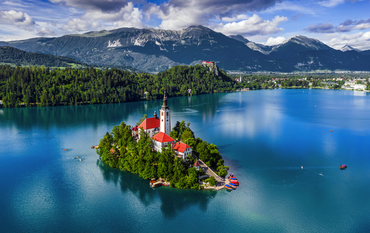 Insel mit Kirche im türkisblauen See, umgeben von Bergen und Wäldern.
