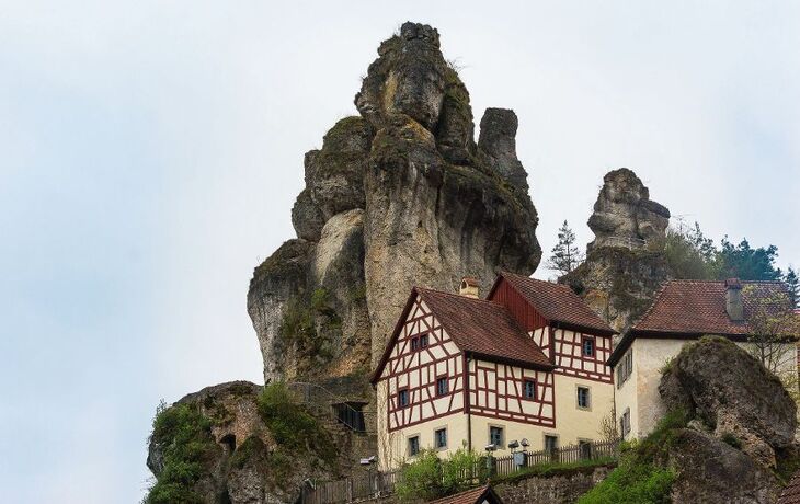 Fachwerkhaus vor einer imposanten Felsformation in einer ländlichen Umgebung.