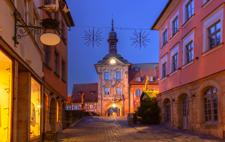 Straße mit historischen Gebäuden und beleuchtetem Rathaus bei Dämmerung