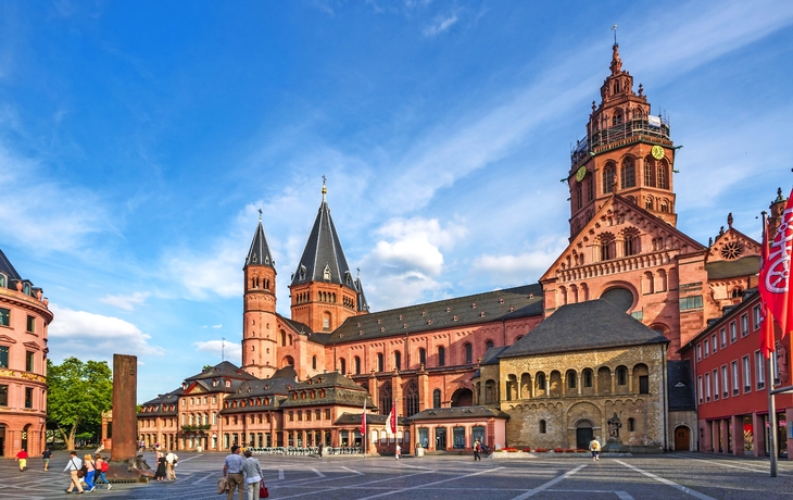 Mainzer Dom bei sonnigem Wetter, umgeben von historischen Gebäuden und Menschen auf dem Platz.