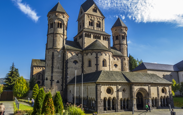 Romanische Kirche mit drei Türmen und blauem Himmel im Hintergrund.