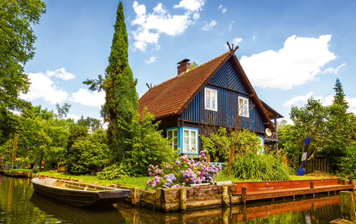 Blaues Fachwerkhaus an einem Fluss mit Blumengarten und Ruderboot.