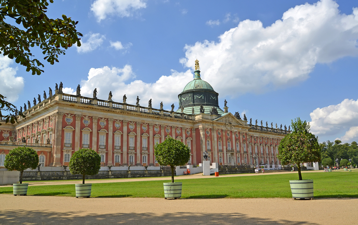 Barockes Gebäude mit Kuppel und Statuen, umgeben von Gartenanlagen.