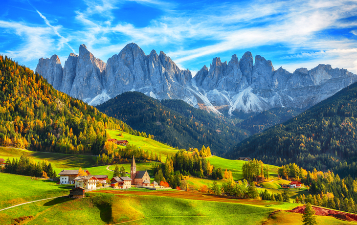Dorf in grüner Landschaft vor Bergkulisse bei klarem Himmel