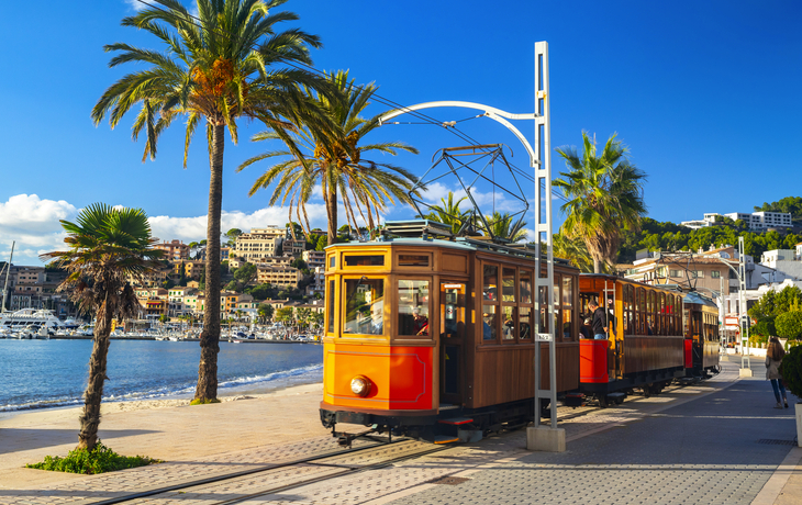 Straßenbahn in Port de Sóller auf Mallorca entlang der Küste mit Palmen im Hintergrund.