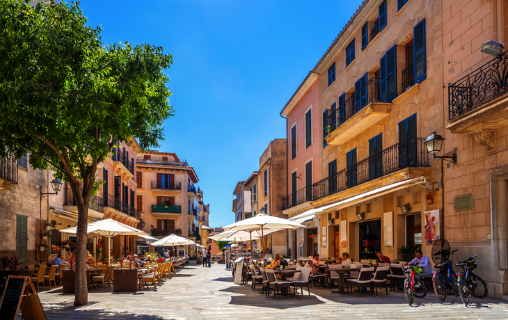 Straßencafé in einer sonnigen europäischen Altstadt mit Menschen und Fahrrädern.