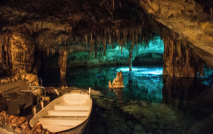 Boot in einer beleuchteten Höhle mit Stalagmiten und Stalaktiten.