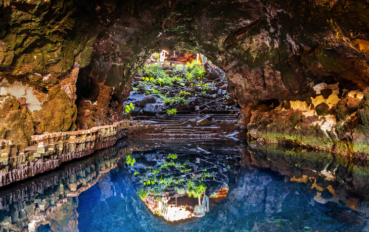 Unterirdische Höhle mit blauem Wasser und Pflanzen an den Felswänden.