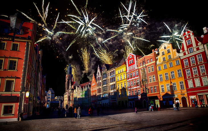 Feuerwerk über einem bunten, historischen Stadtplatz bei Nacht.