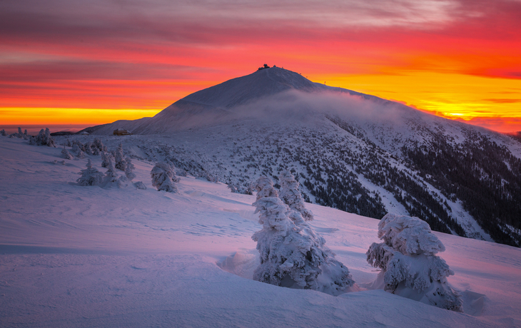 Winterlandschaft mit schneebedecktem Berg bei Sonnenuntergang.