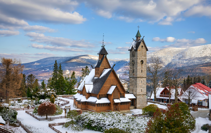 Holzkirche im Schnee mit Bergen im Hintergrund.