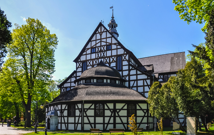 Fachwerkkirche umgeben von Bäumen bei sonnigem Himmel.