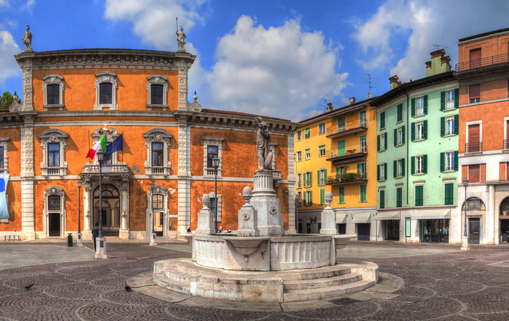 Wunderschöner historischer Platz mit Brunnen und bunten Gebäuden bei blauem Himmel.