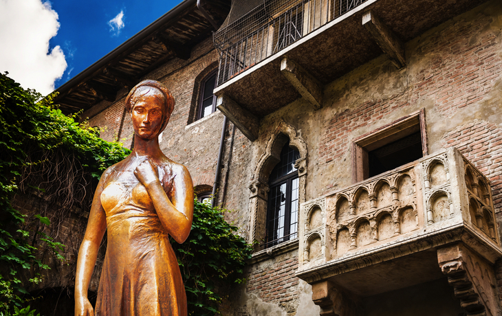 Statue einer Frau vor einem historischen Gebäude mit Balkon und Efeu.