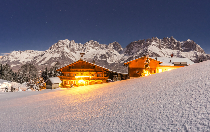Schneebedeckte Berghütten vor einer Bergkulisse bei Nacht.