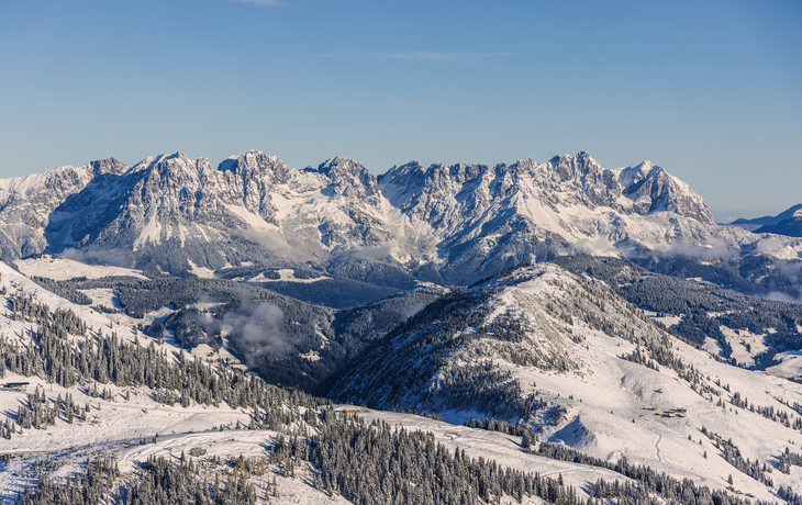 Verschneite Berglandschaft mit klarer Sicht auf das Gebirgsmassiv unter blauem Himmel.