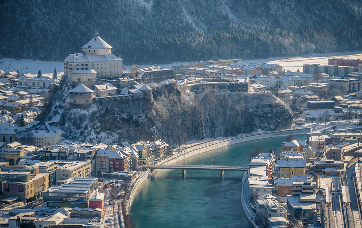 Stadt mit Schloss und Fluss in winterlicher Landschaft.