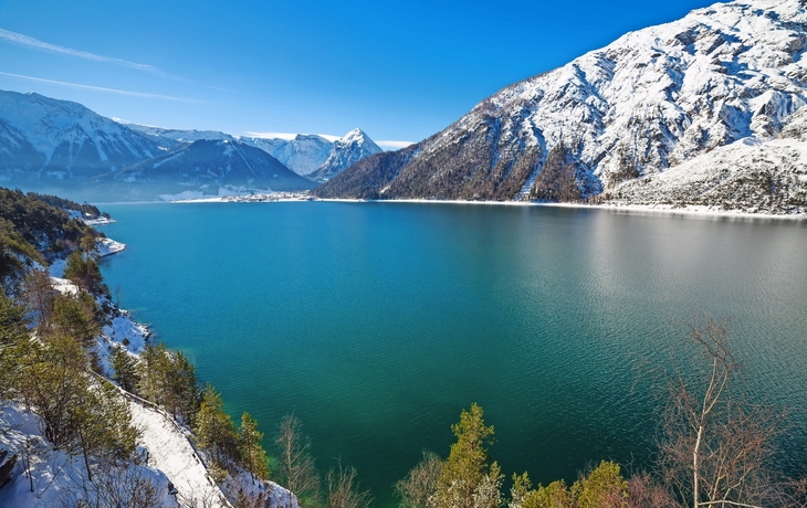 Bergsee umgeben von schneebedeckten Bergen unter blauem Himmel.