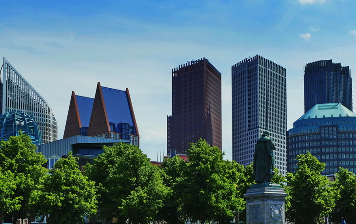 Moderne Skyline mit Bäumen und Statue im Vordergrund.