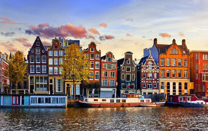 Gracht in Amsterdam mit traditionellen Häusern und Hausbooten bei Sonnenuntergang