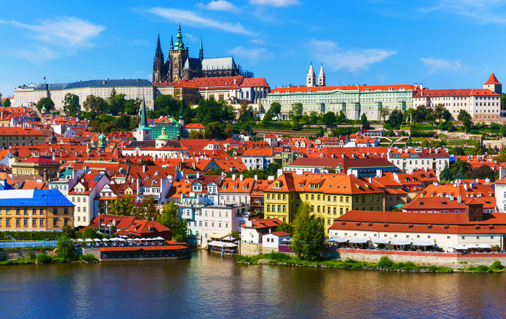 Blick auf die Prager Burg und roten Dächer der Altstadt am Flussufer.