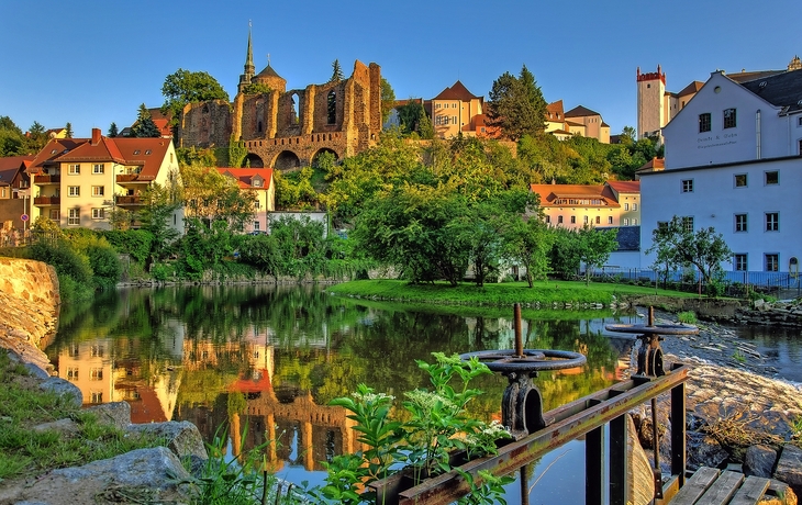 Ruine der Nikolaikirche in Hammermühle im Sommer, umgeben von Grün und Wasser.